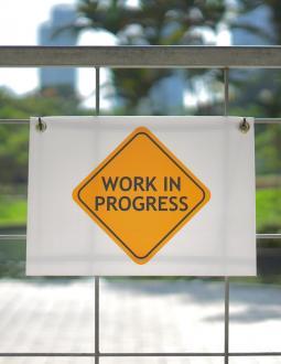 Sign hanging on a fence that reads "Work in Progress"